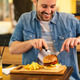 Man smiling and cutting into burger with fork and knife